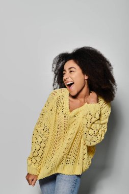 Kıvırcık saçlı genç bir kadın canlı sarı bir kazak giyerken ışıl ışıl gülümsüyor.