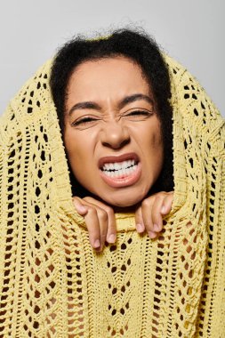 A young woman playfully grimaces while wrapped in a vibrant yellow sweater, showcasing her lively spirit. clipart