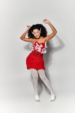 A vibrant young woman wears a chic red dress with feathers, playfully posing and expressing joy. clipart