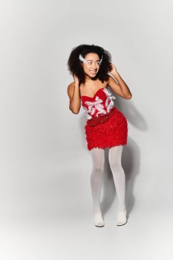 A young woman with curly hair joyfully poses in a striking red feathered skirt, bringing vibrancy to a soft grey background. clipart