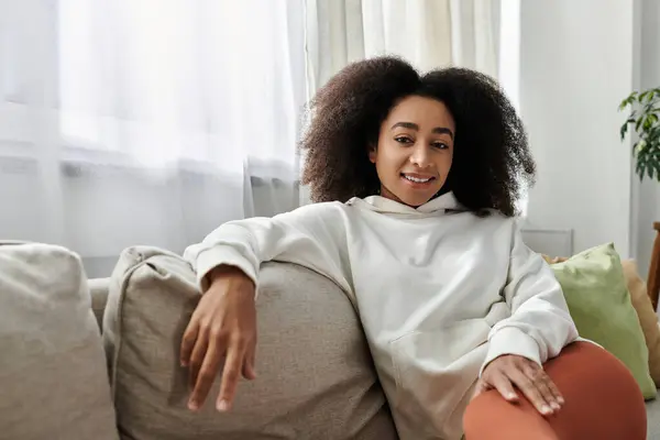 stock image A young woman relaxes in her cozy attire, smiling comfortably in her living room.