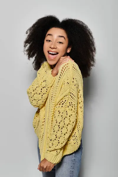 Stock image A joyful African American woman with curly hair wears a cozy yellow sweater and beams with happiness.