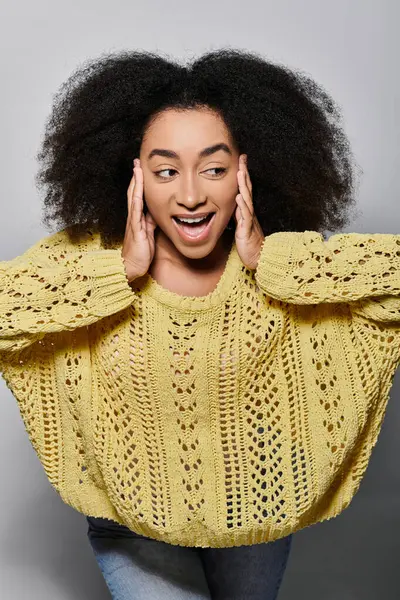 stock image A vibrant young woman with curly hair smiles widely, showcasing excitement in her stylish yellow sweater.