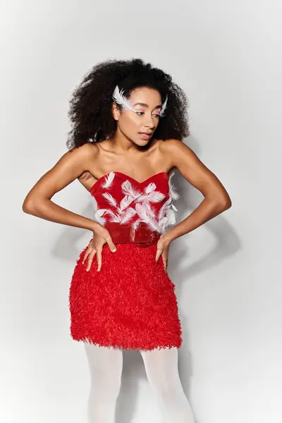 stock image A stylish young woman strikes a pose in a striking red outfit with feather accents, exuding confidence.