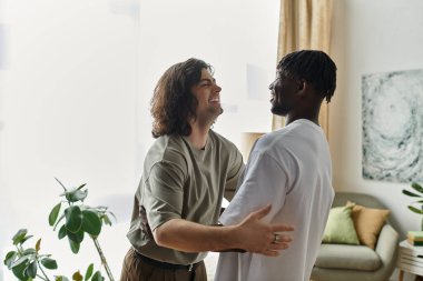 Bitkilerle dolu, aydınlık ve davetkar bir oturma odasında iki adam neşeli bir kucaklaşmayı paylaşıyor..