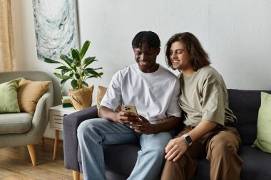 Two partners cuddle on the couch, sharing laughter and a meaningful moment while using a smartphone. clipart