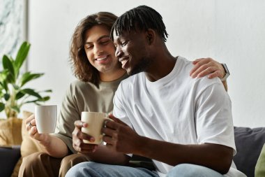 A loving couple shares warmth and laughter while sipping tea on a comfortable couch. clipart