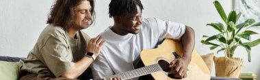 Bir çift evlerinde gitar çalarken koltuğa oturup kahkahalarını paylaşıyor..
