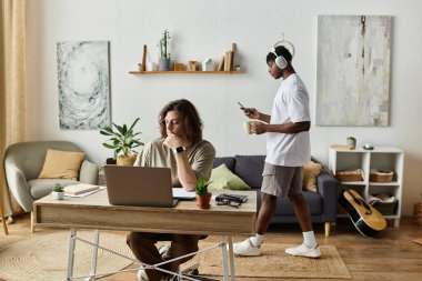 İki ortak evde sıcak bir anı paylaşıyor, biri işe odaklanmış, diğeri müziğe dalmış..