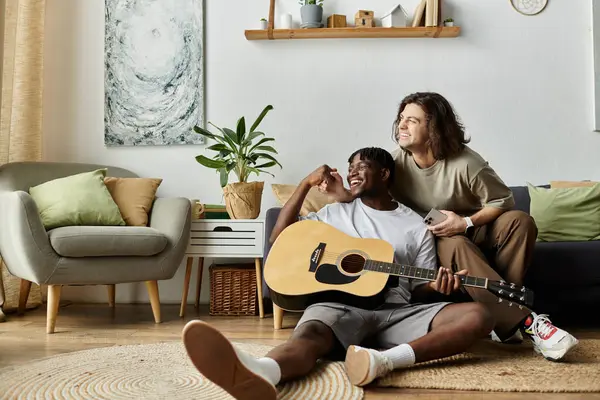 stock image A couple relaxes at home, sharing laughter while playing guitar together.