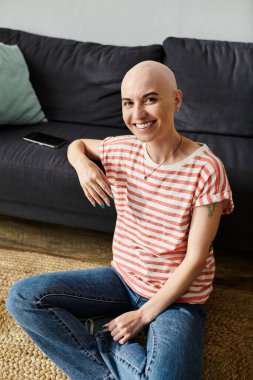 A cheerful bald woman sits comfortably on the floor, showcasing her confident spirit. clipart