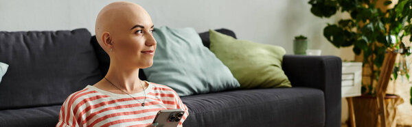 A calm young woman with alopecia smiles while using her smartphone indoors.
