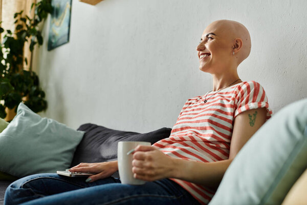 Веселая лысая женщина наслаждается мирным моментом, потягивая теплый напиток на своем диване.