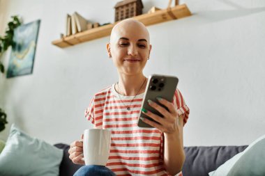 Neşeli, kel bir kadın, akıllı telefonuyla meşgulken kahvenin tadını çıkarıyor..