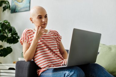 Alopecia hastası genç bir kadın rahatça otururken dikkatle dizüstü bilgisayarına bakar..