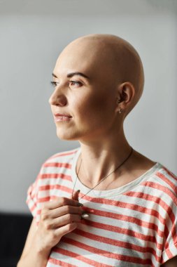 Genç kel bir kadın düşünceli bir şekilde duruyor, güzelliğini ve gücünü nazik ışığa karşı gösteriyor..