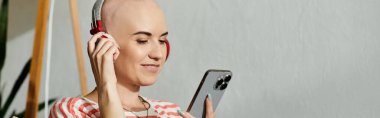 A young woman with alopecia smiles as she listens to music on her phone, enjoying her moment. clipart