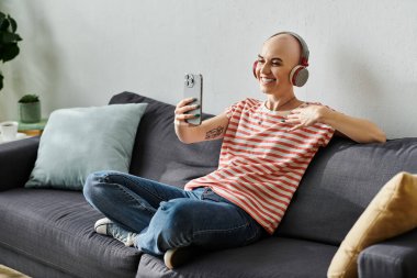 Alopecia hastası neşeli genç bir kadın koltukta rahatça oturur ve neşeli bir video görüşmesi yapar..