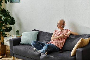 Alopecia hastası kel bir kadın kendini müziğine kaptırmış bir koltukta rahatça oturur..