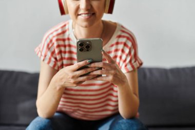 Neşeli bir gülümsemesi olan genç bir kadın akıllı telefonuyla kulaklık takıyor..