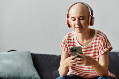 A beautiful young woman, bald from alopecia, relaxes on her couch, listening to music. clipart