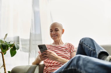 Kel bir kadın telefonuyla kayarken, gün ışığında sırılsıklam gülümsüyor..