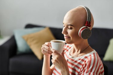 A young beautiful bald woman with alopecia savors a cup of coffee while relaxing at home. clipart