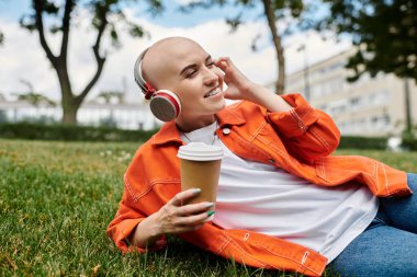 Çimlere uzanmış, müzik dinlerken kahvesini yudumlayan neşeli, genç bir kadın..