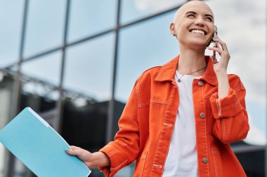 Neşeli, kel bir kadın neşeli bir telefon görüşmesi yaparken gülümsüyor..