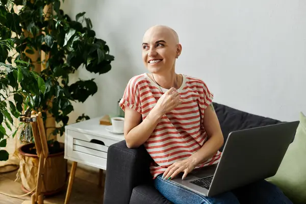 stock image A cheerful bald woman smiles while using her laptop in a warm, inviting home setting.