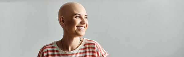 Радостная лысая женщина ярко улыбается, обнимая свою неповторимую красоту в спокойной обстановке.