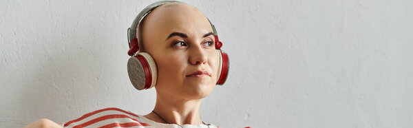 Красивая лысая женщина наслаждается музыкой в наушниках, подчеркивая свою неповторимую красоту и стиль.