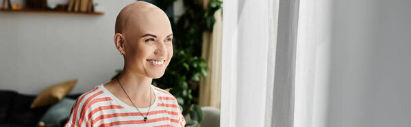 Молодая женщина с лысой головой излучает позитив стоя у окна.