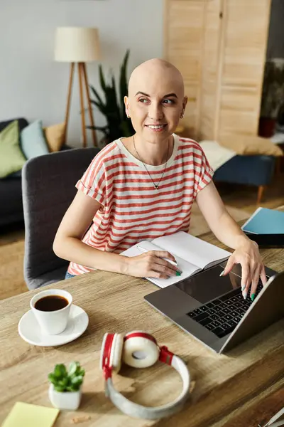 stock image A woman with a joyful expression sits at her desk, typing on a laptop while planning her day.