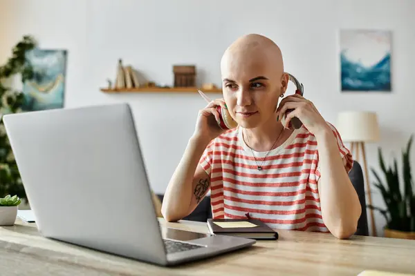 stock image A confident woman wears headphones while focused on her laptop during a virtual meeting.