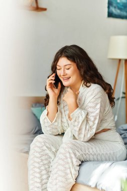 Genç ve iri yarı bir kadın, neşeli bir telefon konuşması yapmaktan zevk alıyor. Gülümsüyor ve evde rahatlıyor..