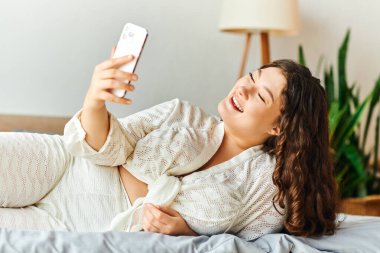 Neşeli, iri yarı bir kadın rahat bir şekilde rahat bir şekilde uzanır ve evinde selfie çeker..