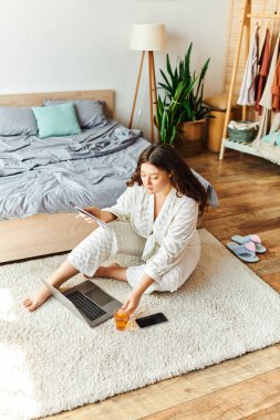 A young plus size woman enjoys a relaxing morning while using her laptop at home. clipart