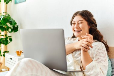 Neşeli, iri yarı bir kadın evde online bir konuşma yaparken ışıl ışıl gülümser..
