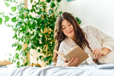 Genç, güzel, iri yarı bir kadın evde kitap okuyarak rahatlatıcı bir öğleden sonranın tadını çıkarıyor..