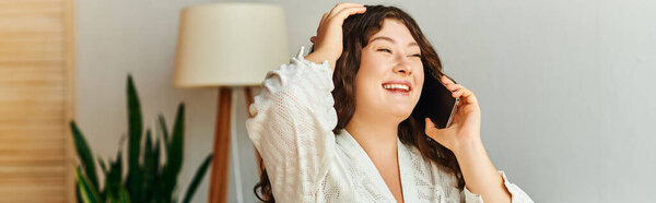 Молодая женщина плюс размер счастливо смеется, разговаривая по телефону в уютной комнате.