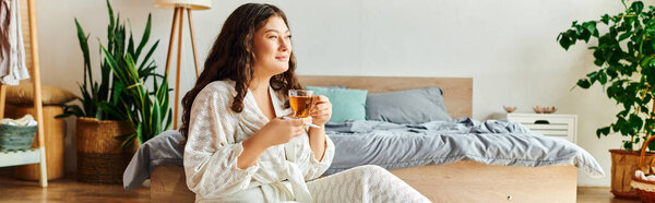 Молодая, красивая, плюс размер женщина расслабляется дома, наслаждаясь чаем в ее уютной спальне настройки.