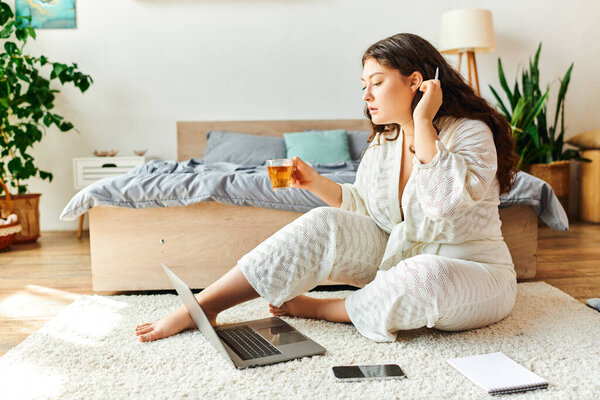 Relaxing at home, a beautiful plus size woman engaged with her laptop and drink.
