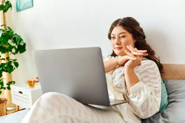 stock image A young plus size woman sits comfortably at home, engaged with her laptop and relaxing thoughtfully.