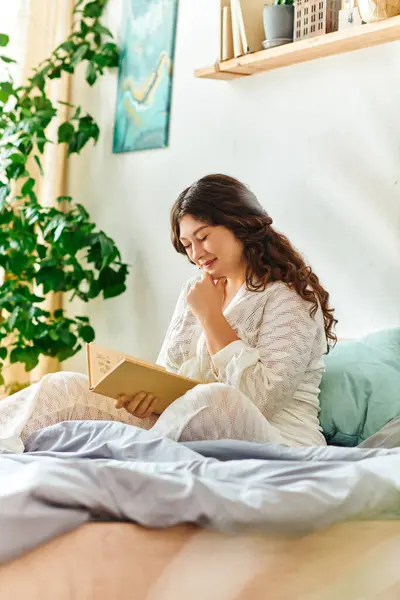 stock image A young plus size woman relaxes on her bed, deeply engaged in reading a book in her cozy room.