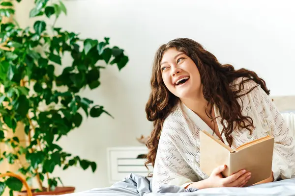 stock image A cheerful plus size woman laughs while reading in her cozy room filled with plants.