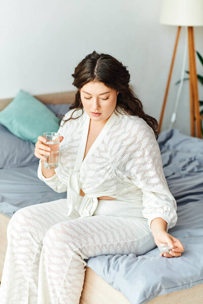 Молодая красивая женщина плюс размер расслабляется дома, потягивая стакан воды, отражая.