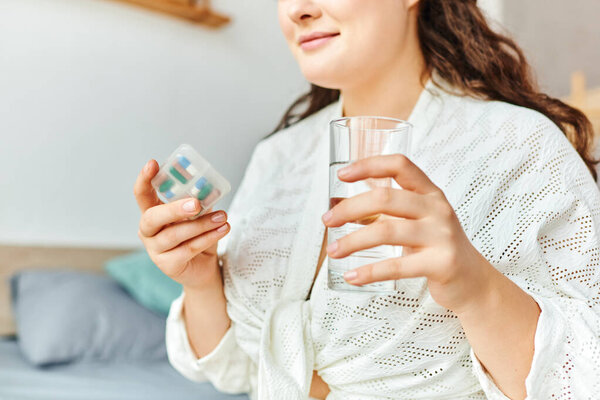 A plus size woman peacefully gets ready to take her morning medications while at home.