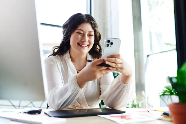 Stock image A plus size woman smiles brightly while browsing her smartphone at office, creating a warm atmosphere.