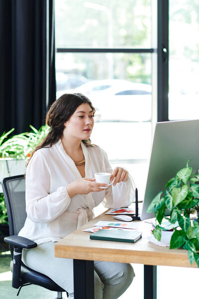 A beautiful young woman sips tea, focusing on her tasks in a cozy workspace at office.